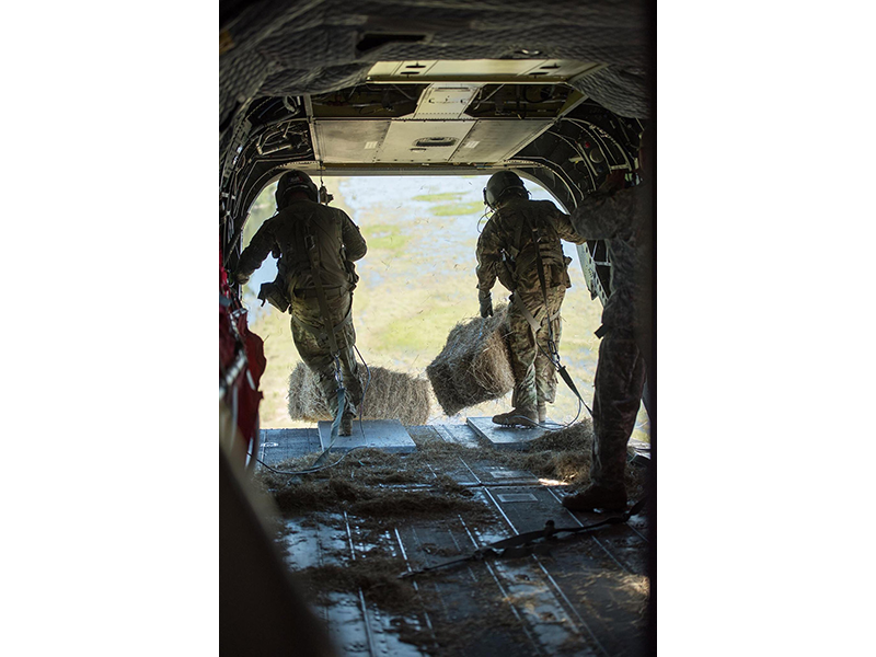 soldiers in the back of a helicopter carrying hay